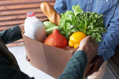 Close up of delivery man handing bag with fresh groceries to client outdoors